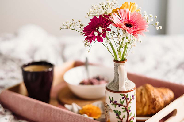 Breakfast in bed with eggs, bacon, waffles, coffee, fruits, and flowers