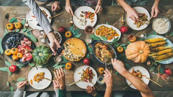 Thanksgiving dinner with lots of food on the table like turkey, corn, mashed potatoes, green beans, pumpkin, pie, and more.