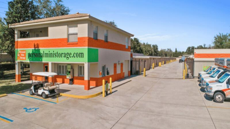 Exterior view of a Personal Mini Storage facility with a main office building, rows of storage units, and U-Haul trucks parked outside, highlighting the brand’s services operating only in mid-Florida