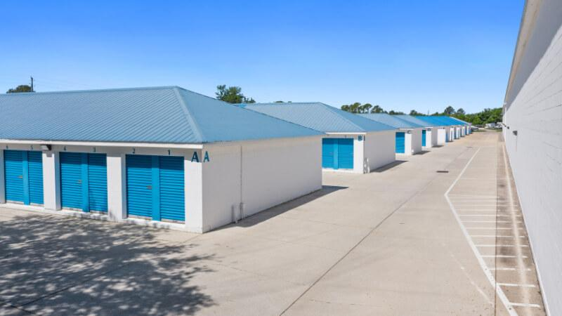 outdoor storage facility with multiple white buildings featuring blue roll-up doors and matching blue roofs, providing secure and organized self-storage units under a clear blue sky