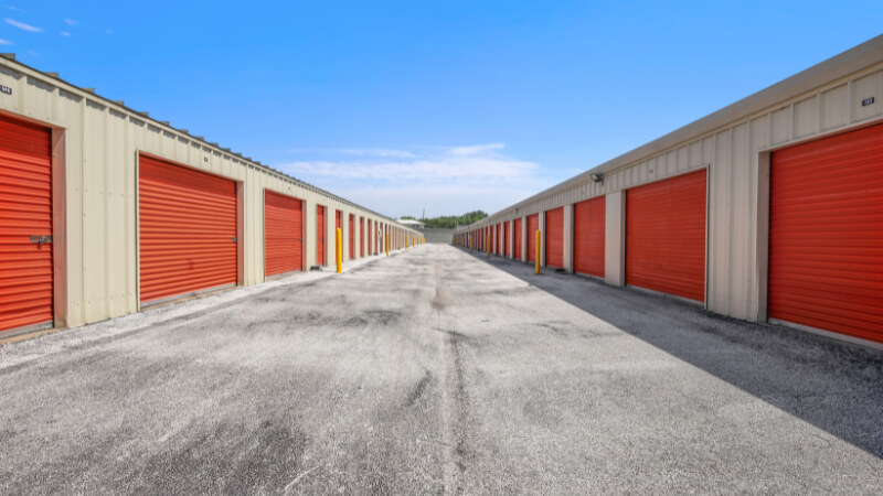 A row of outdoor storage units with bright red doors aligned on a concrete path under a clear blue sky, conveying a sense of organization and spaciousness.