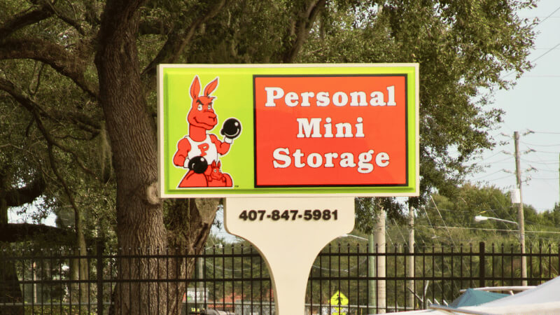 Sign for "Personal Mini Storage" features a red kangaroo in boxing gloves. Set against trees, it conveys a strong, reliable vibe. Contact number below.