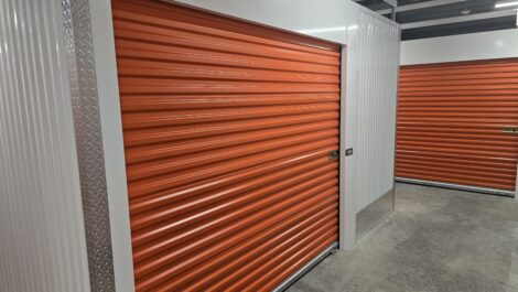 Indoor self-storage units with roll-up metal doors, concrete floors, and bright overhead lighting
