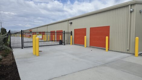 Ground-floor drive-up storage units with roll-up doors, security gate, and wide concrete access at a self-storage facility.