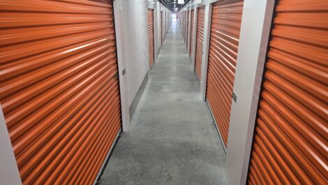 Interior self-storage hallway with multiple roll-up metal doors, concrete flooring, and bright overhead lighting